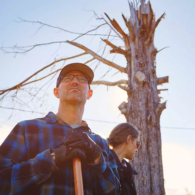 man with shovel and dead tree in background
