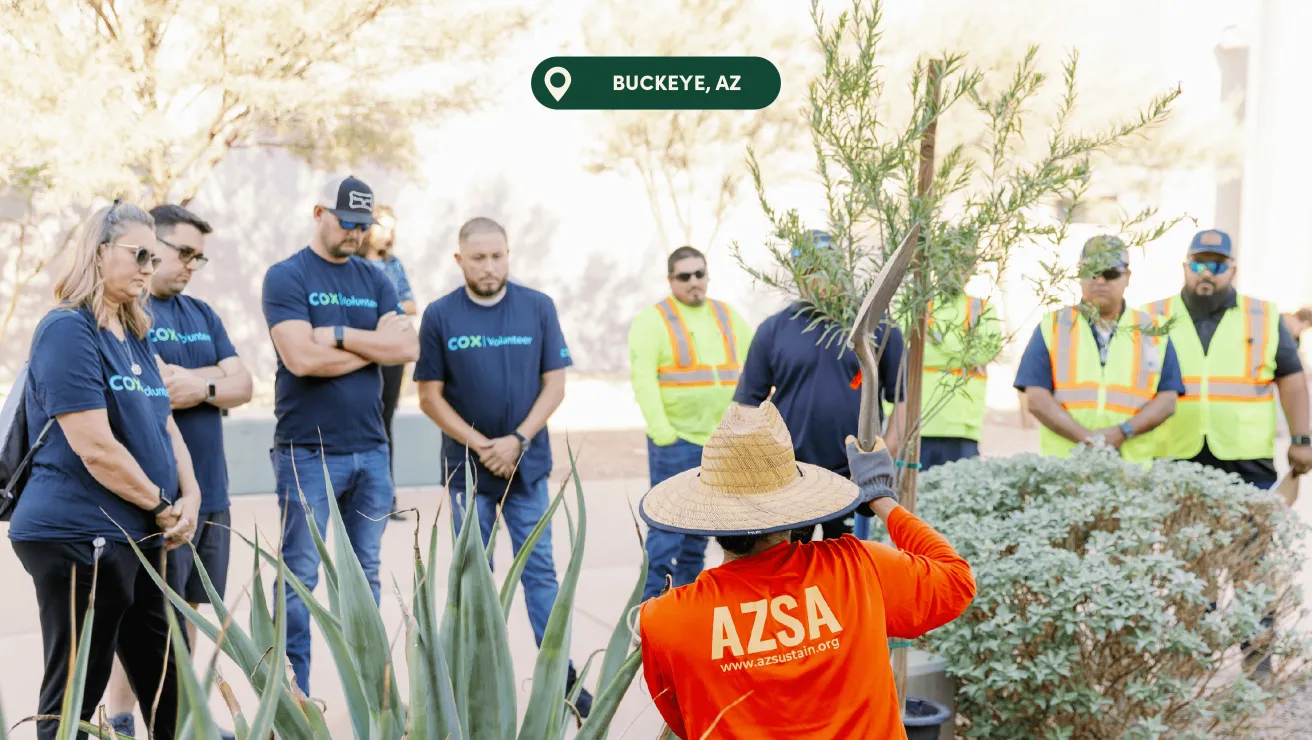 A group of volunteers in matching shirts gathers for a planting activity in Buckeye, AZ, with a focus on community service.