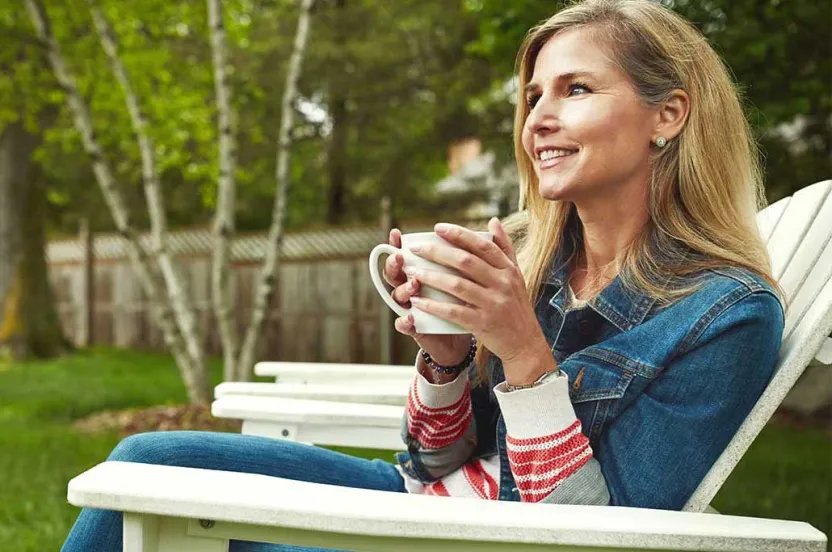 Woman sitting in a chair in her backyard enjoying a cup a coffee.