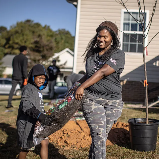 A woman and a child carrying a bag of soil to plant trees in a neighborhood.