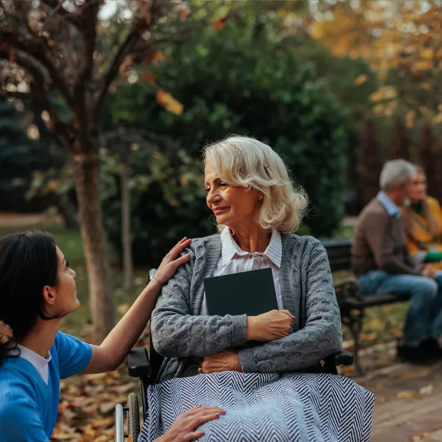 female health care worker talking to elderly patient in wheelchair outside in beautiful garden