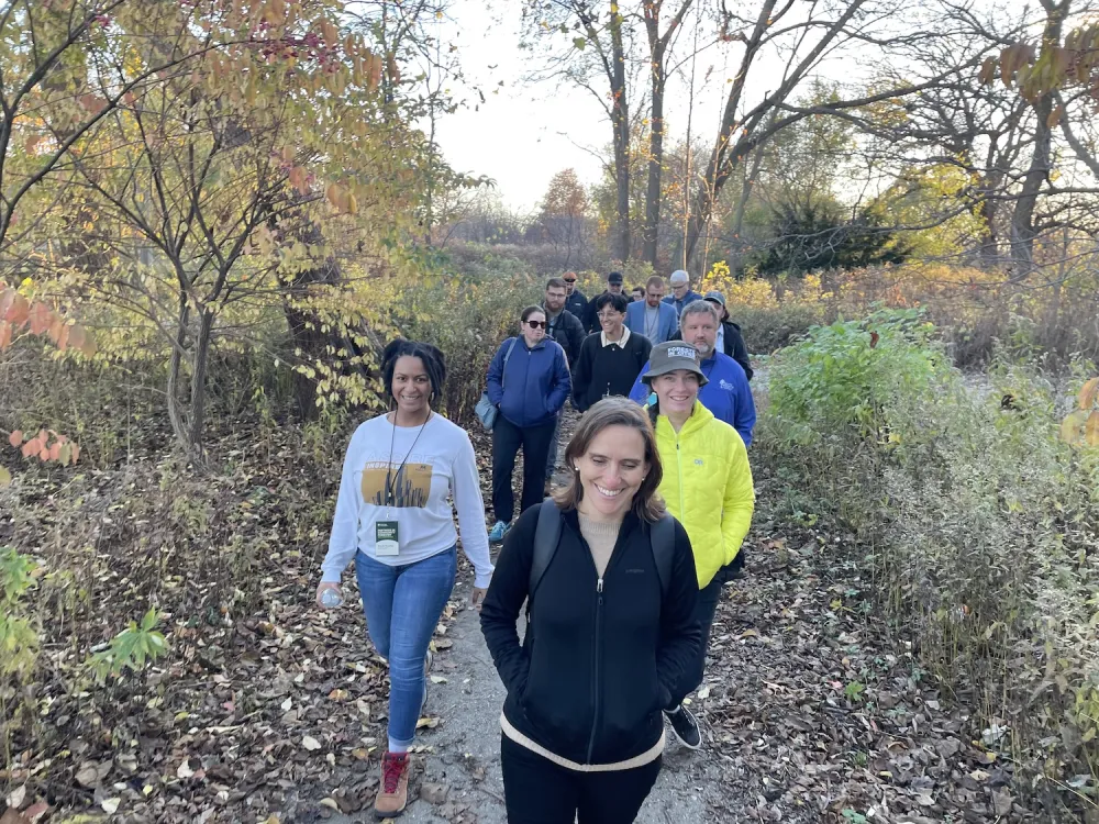 A group of people walking along a wooded trail, surrounded by trees and natural scenery.