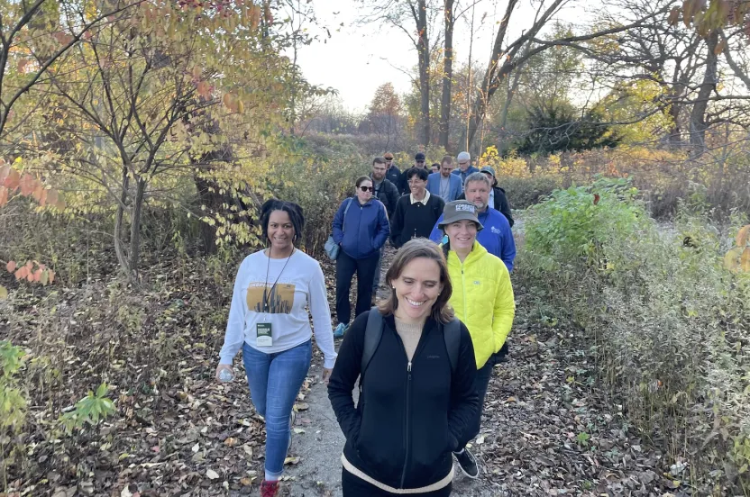 A group of people walking along a wooded trail, surrounded by trees and natural scenery.