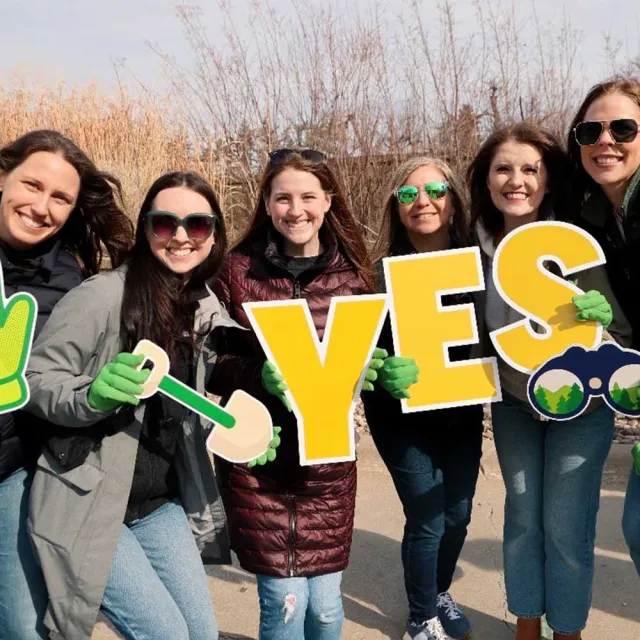 Group of individuals holding colorful signs that read "YES," along with gardening tools, celebrating an environmental initiative.
