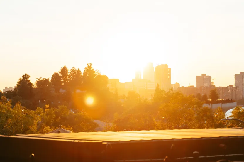 A vibrant sunset over a city skyline, casting warm light on trees and buildings, creating a serene evening atmosphere.