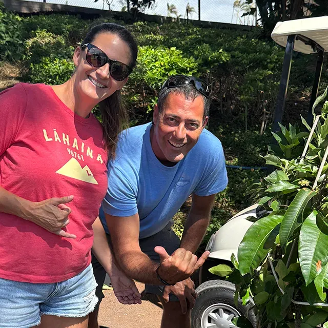Man and woman posing for a photo in front of Hawaii foliage