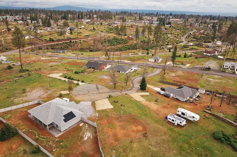 Aerial view of a suburban area with scattered homes and open land patches. A cloudy sky looms above. RVs are parked near some houses. Tranquil atmosphere.