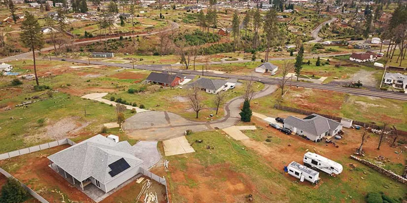 Aerial view of a suburban area with scattered homes and open land patches. A cloudy sky looms above. RVs are parked near some houses. Tranquil atmosphere.