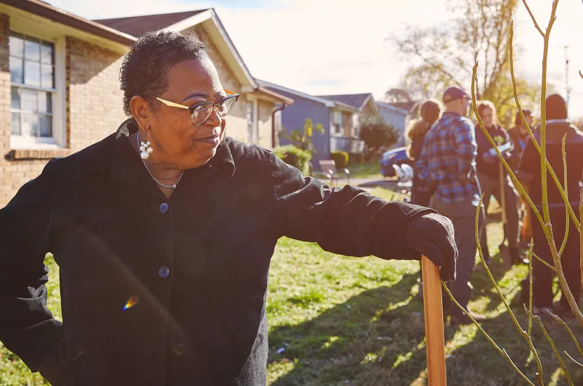 woman resting hand on her shovel, tree-planting volunteers in the background.