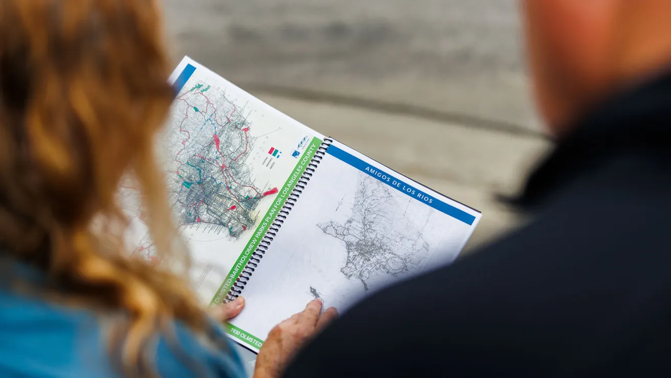 Over the shoulder view of a map of Los Angeles, woman pointing at areas affected by fire. 