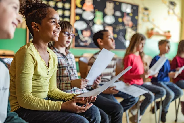 students in a music room holding sheet music and smiling.