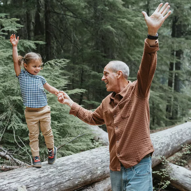 man and grandchild walking on fallen log in forest