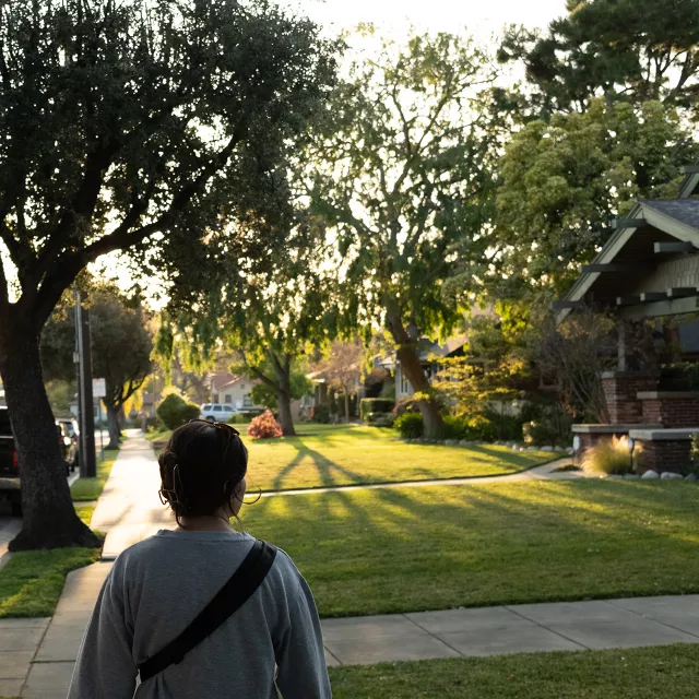 woman wallking on sidewalk in tree-lined neighbhorhood.
