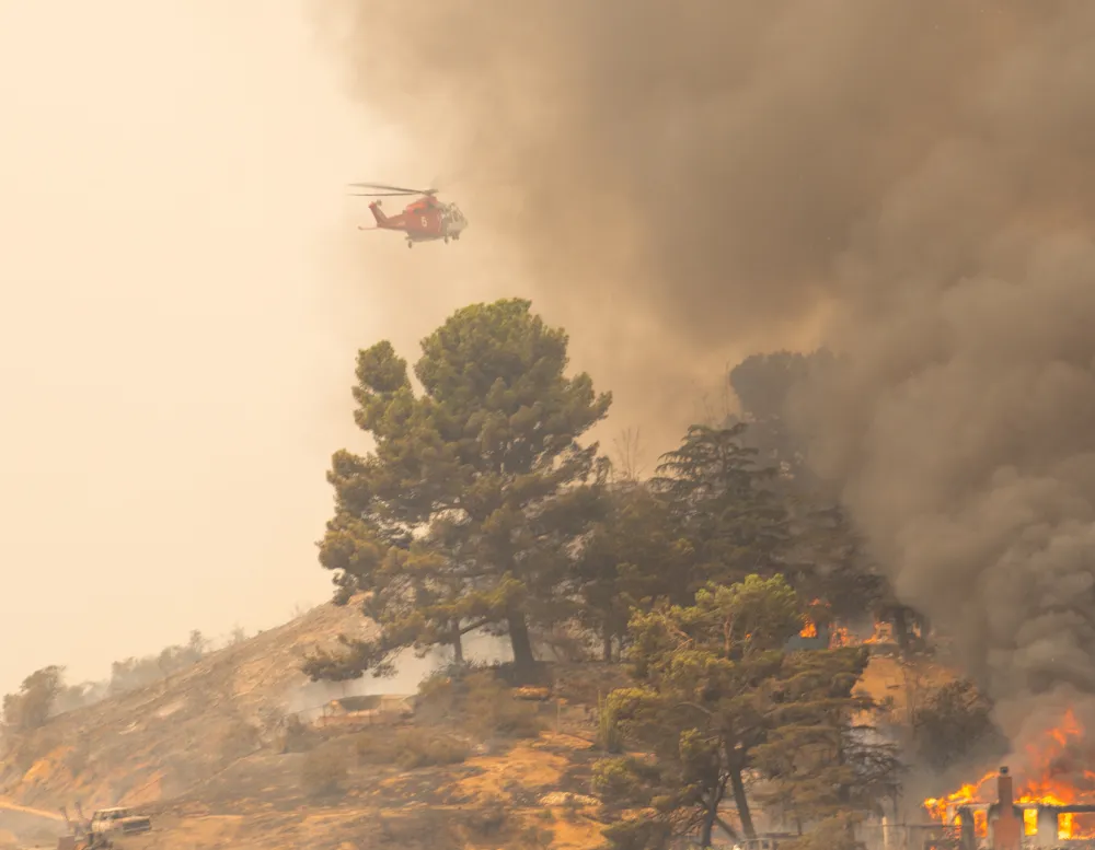 Helicopter dropping water onto fire burning trees and homes.